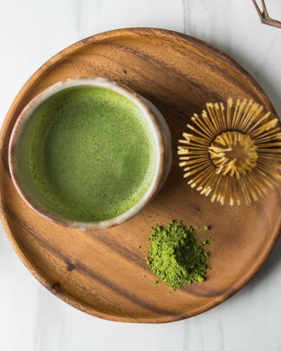 A bowl of whisked matcha with a bamboo chasen and matcha powder on a wooden tray