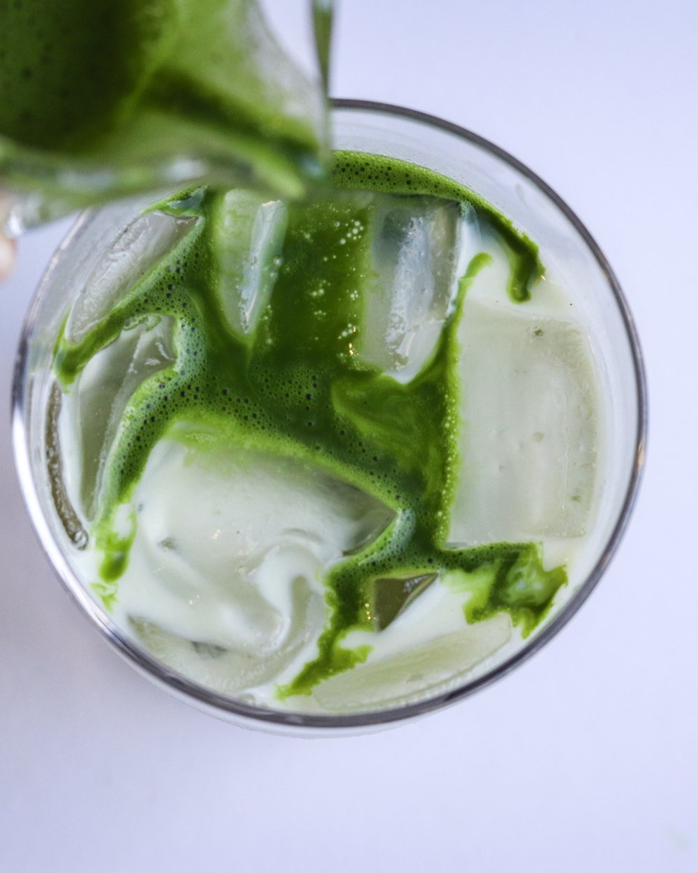 Matcha poured from a jug over an iced latte, seen from above